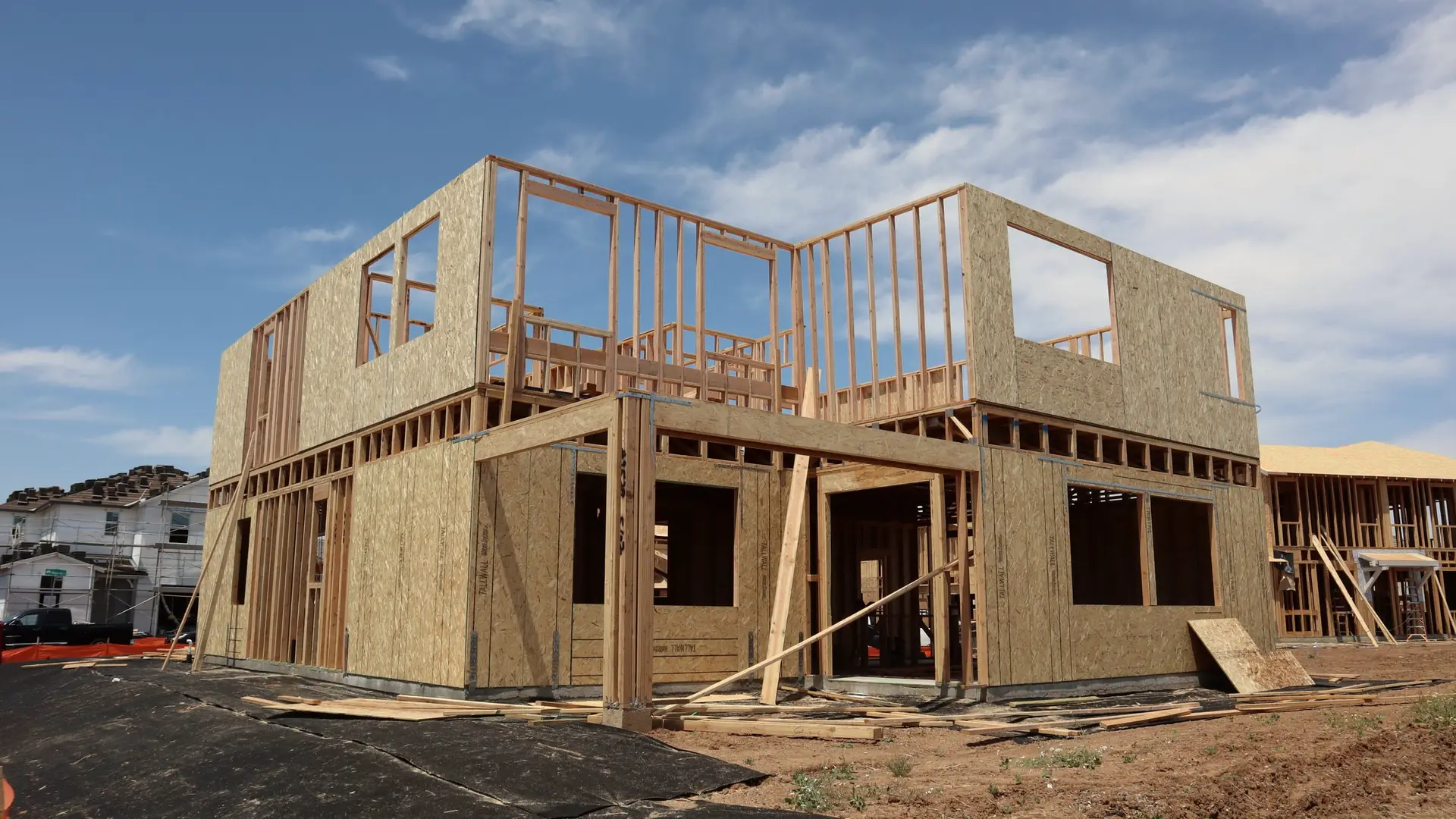 Two-story house framed in lumber and sheathing under a clear sky