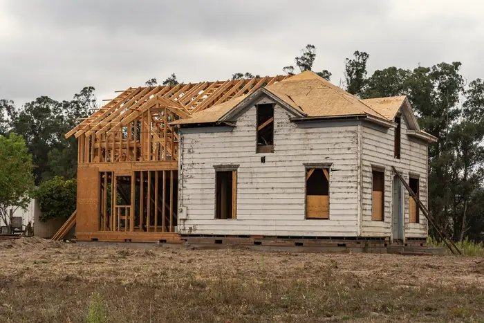 Two-story wood-framed addition rising beside an older white clapboard house