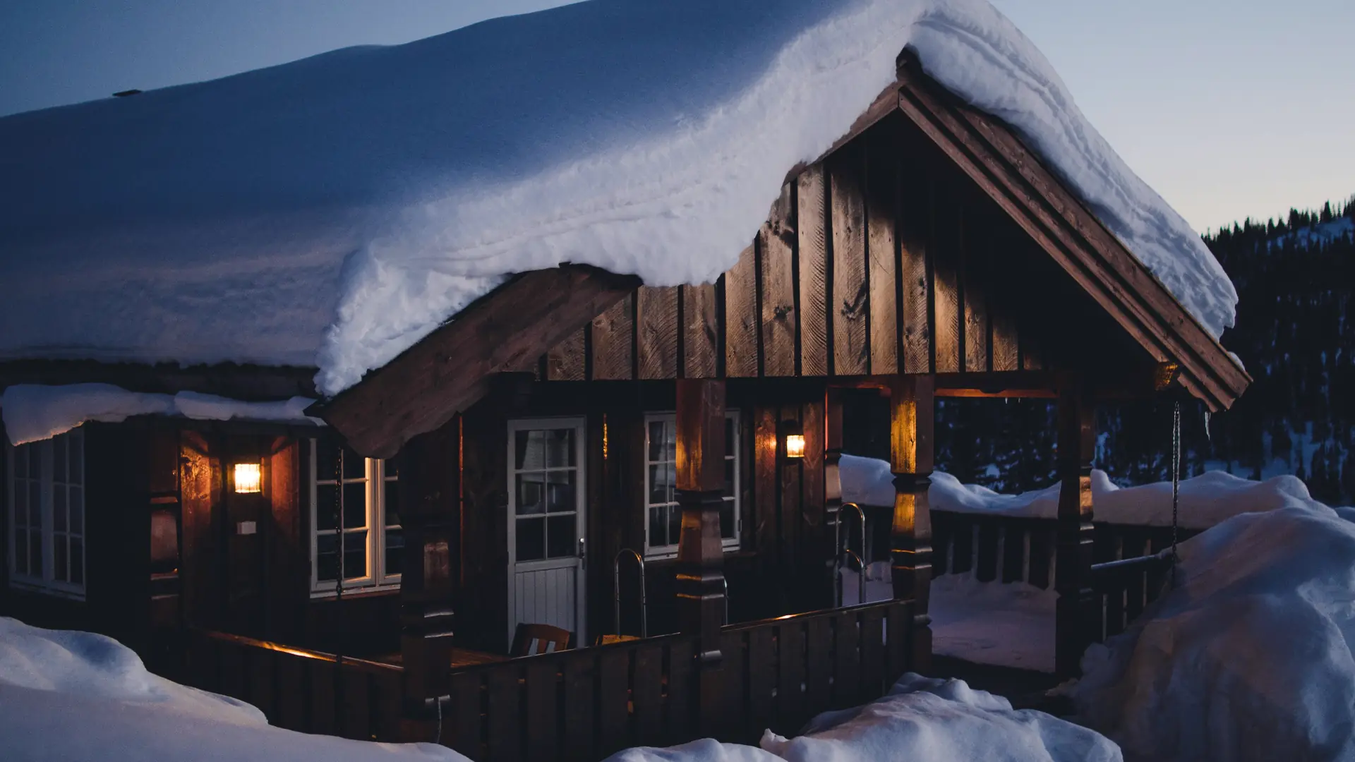 Snow-covered cabin at dusk with warm lights on the porch