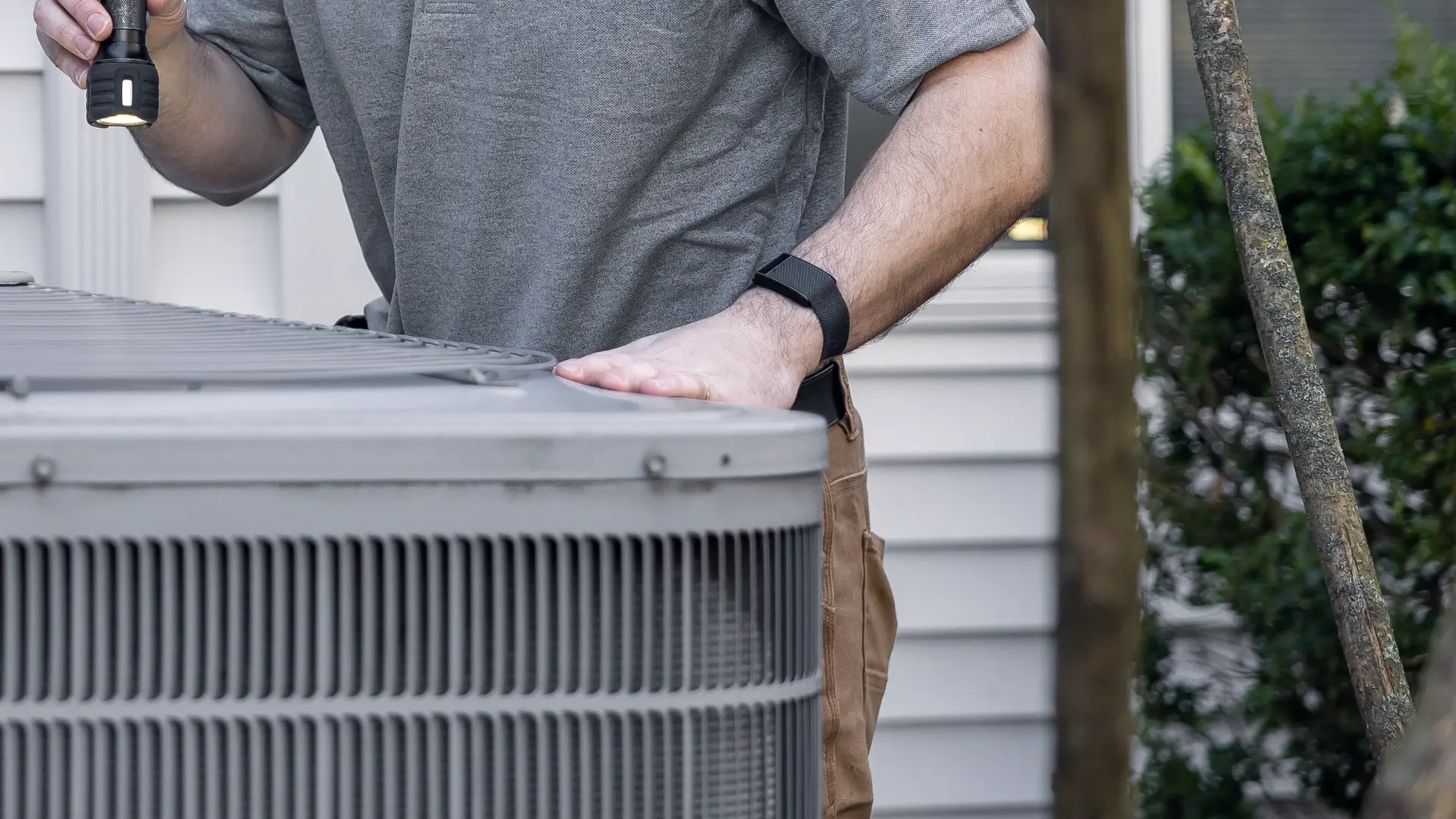 Technician checking an outdoor AC condenser beside a house