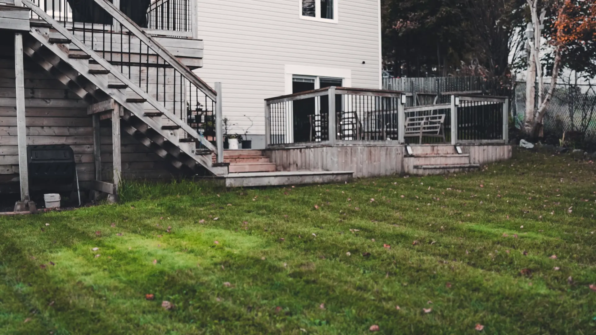Backyard lawn with fresh mow stripes and a few fall leaves below a wooden deck