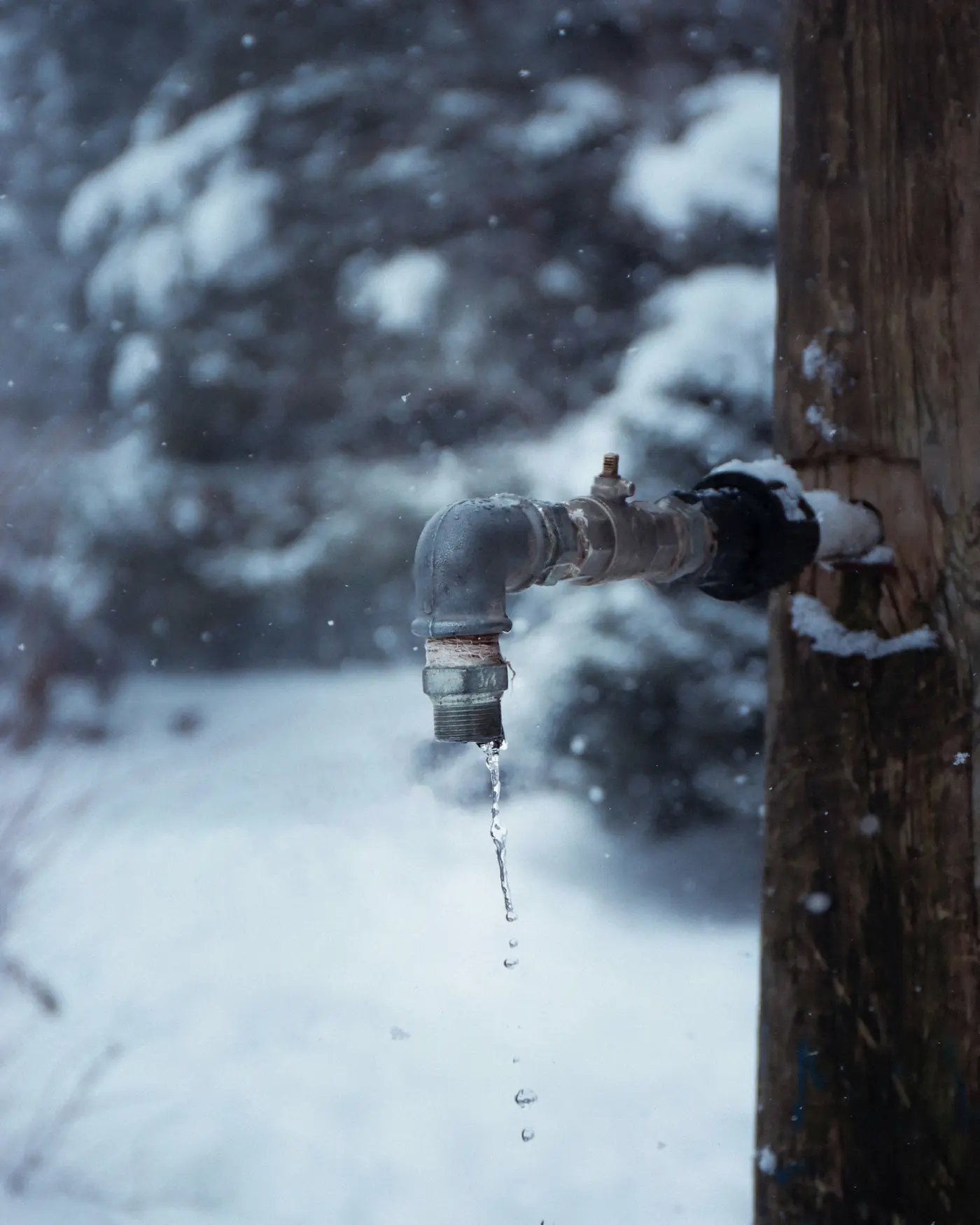 An outdoor spigot dripping in falling snow