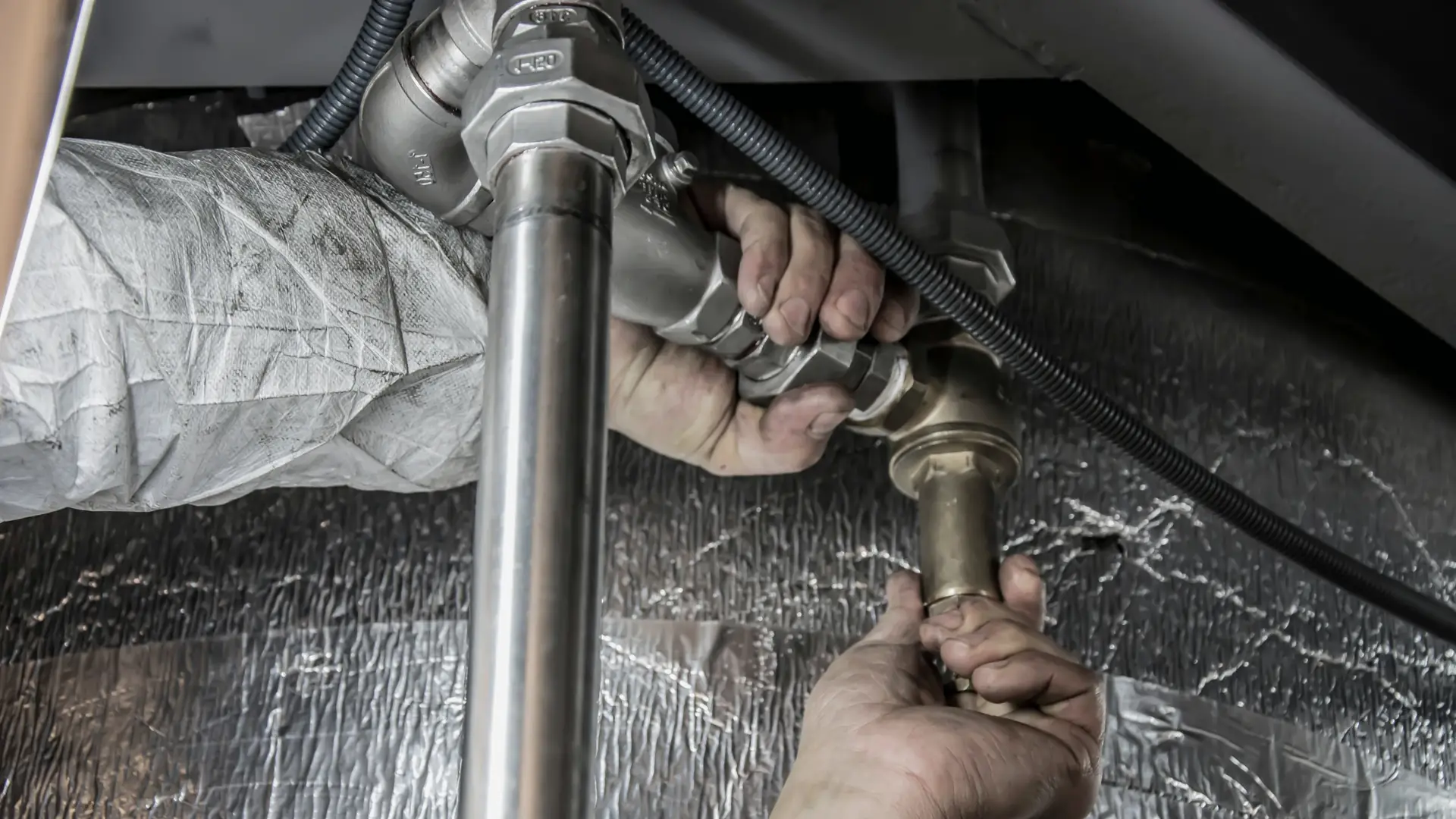 A plumber's hands tightening a fitting on a water line