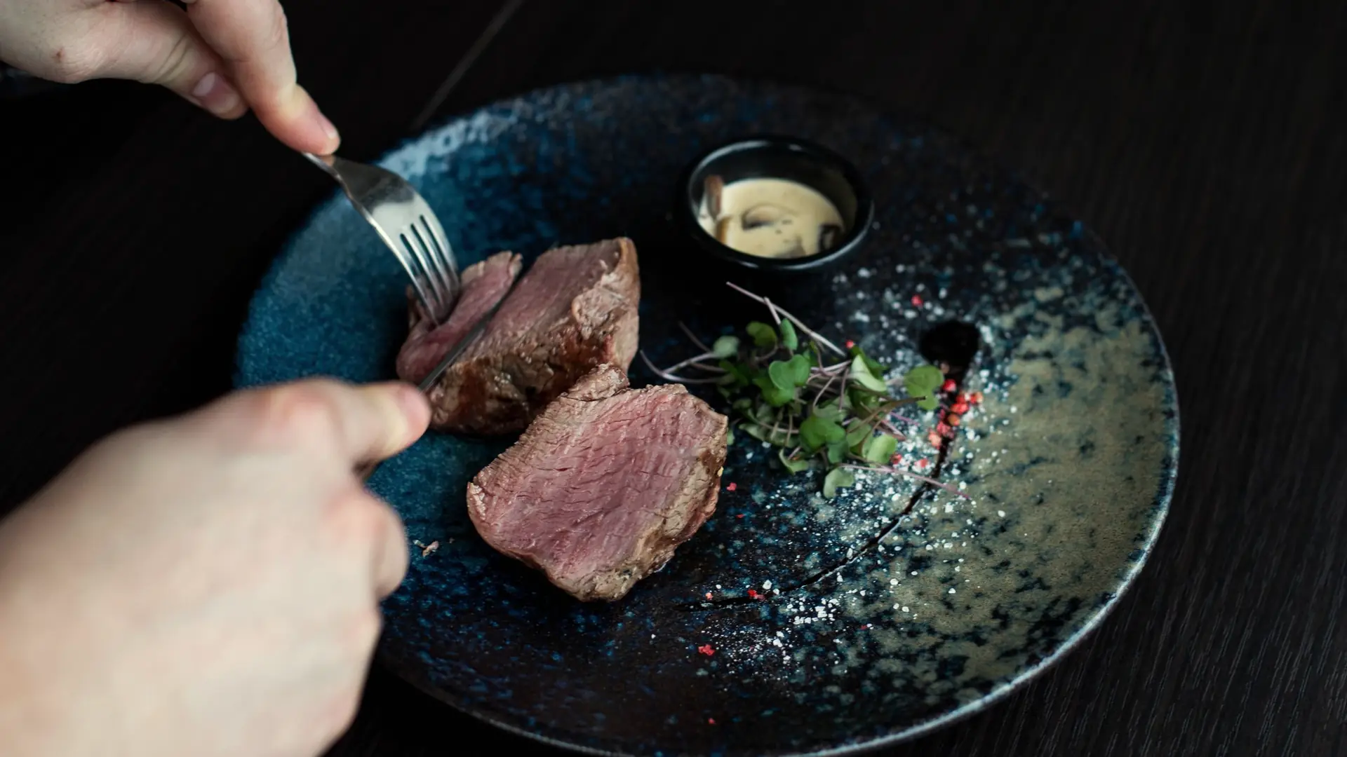 Sliced steak on a dark plate with a small dish of sauce