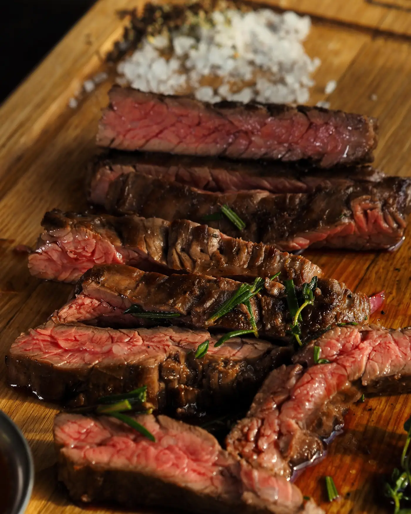Sliced steak, pink in the middle, on a wooden board with coarse salt