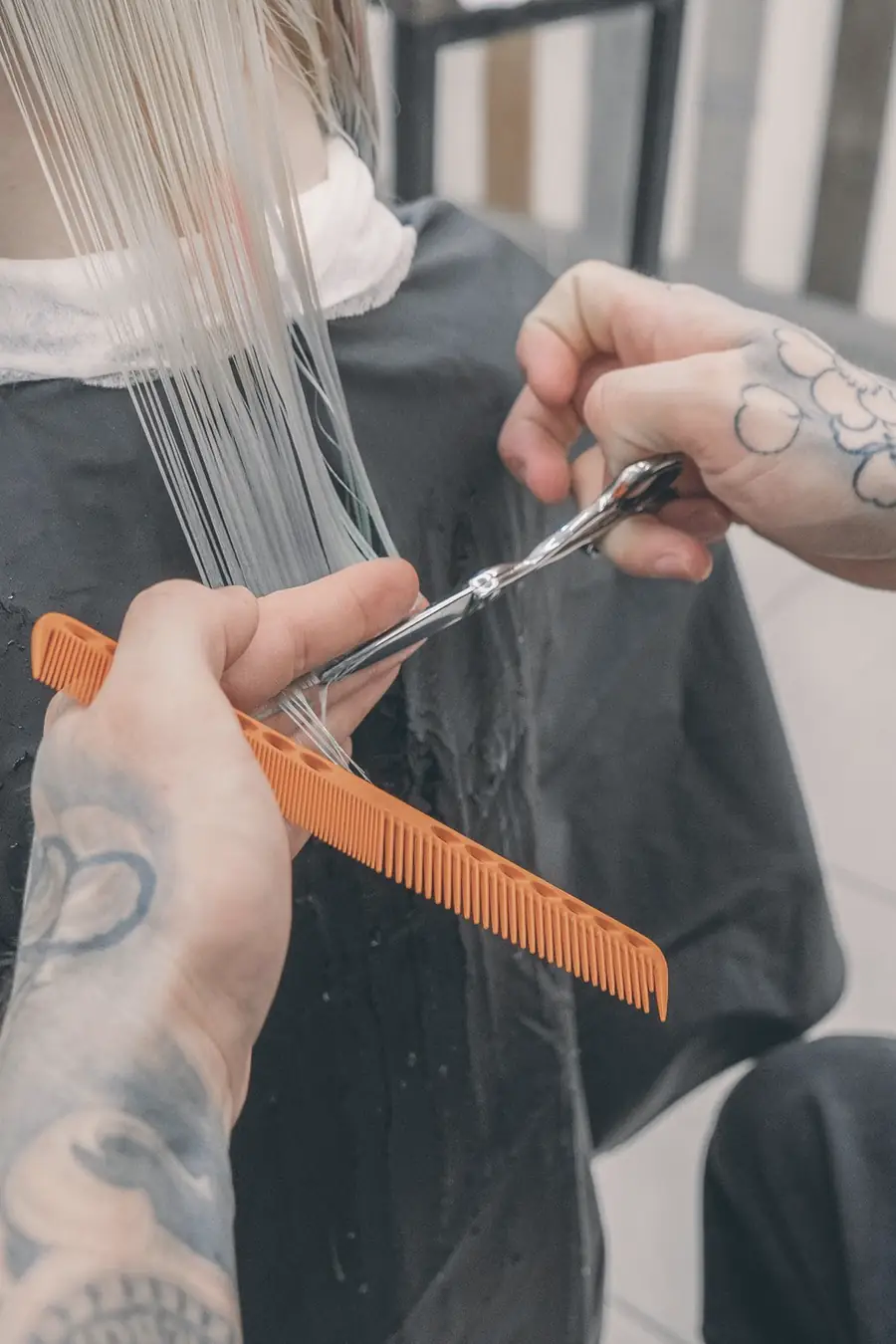 Tattooed hands cutting a straight line through wet platinum hair