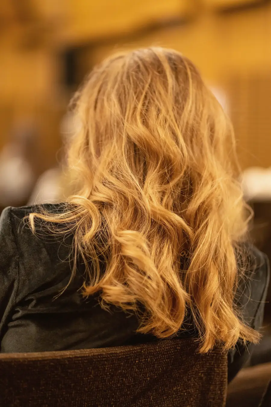 Long golden copper waves seen from behind in warm salon light