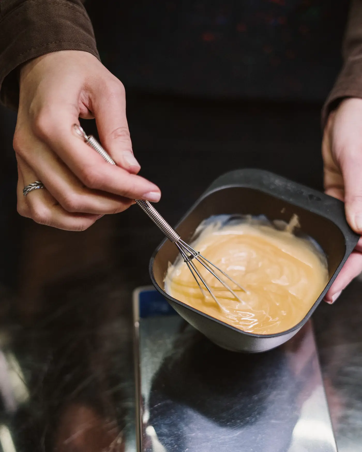 A colorist whisking warm blonde color in a mixing bowl
